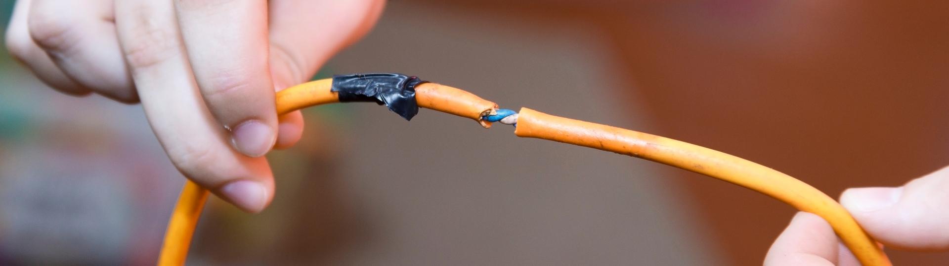 Man holds a frayed, orange extension cord.